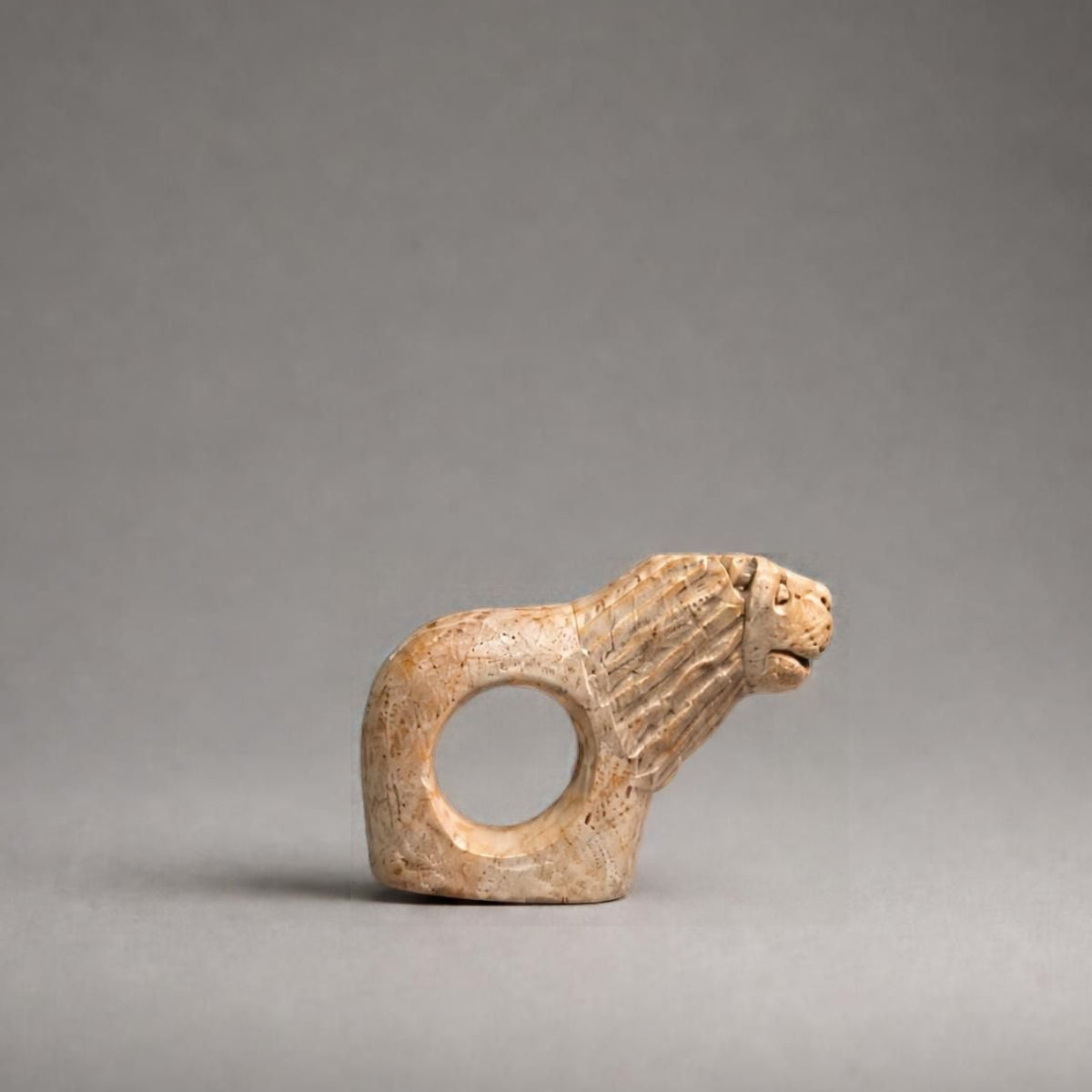 A small carved animal-shaped ring, resembling a stylized dog or fox head with a circular cutout, shown on a smooth gray studio background.