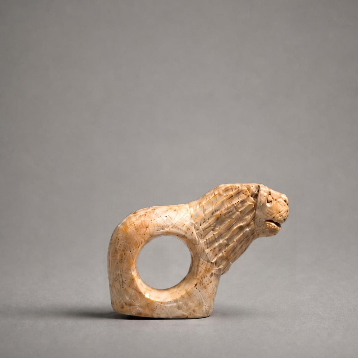 A small carved animal figurine with a ring cutout through its body, shown on a smooth gray studio background.