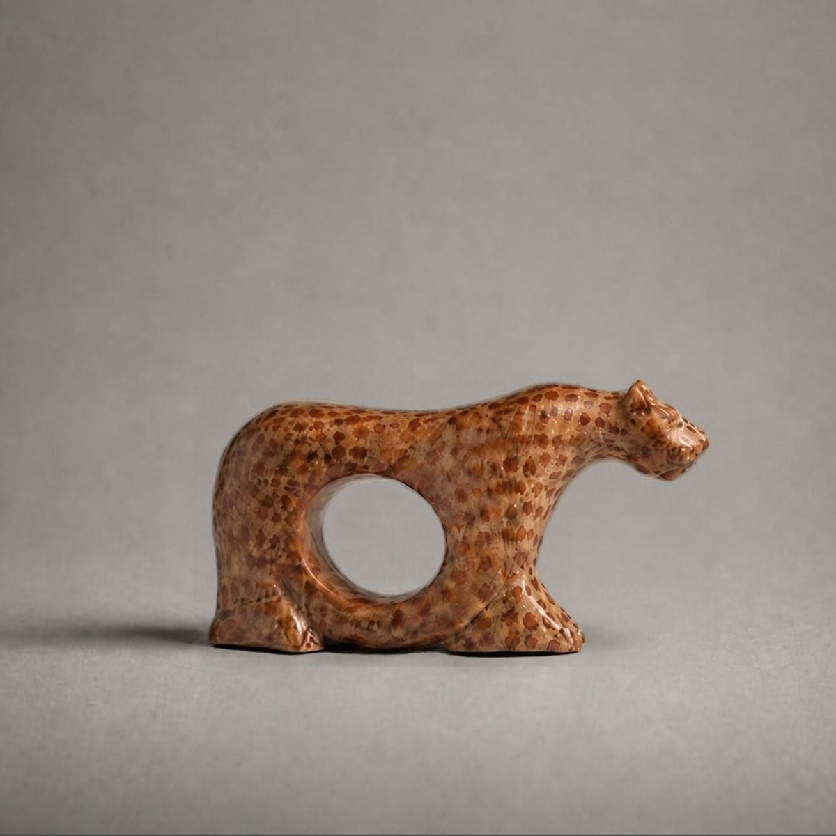 A small carved figurine of a cheetah with a circular cutout in its body, shown on a neutral gray background.