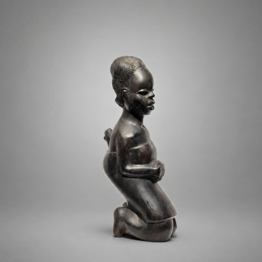 A dark wood sculpture of a kneeling child in profile, shown against a neutral gray studio background.